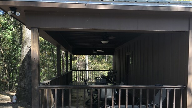 A covered outdoor area with a wooden deck, metal railing, and a planter with flowers.