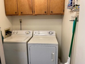A laundry area with two washing machines and wooden cabinets above. - Renovated Ocean-View 3BR at Pelican's Landing (Myrtle Beach)