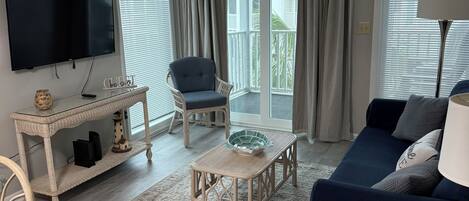 A living room with a flat-screen TV, wicker furniture, a blue sofa, and a view to the outside.