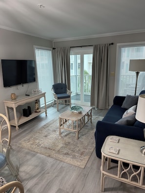 A living room with a flat-screen TV, wicker furniture, a blue sofa, and a view to the outside. - Renovated Ocean-View 3BR at Pelican's Landing (Myrtle Beach)
