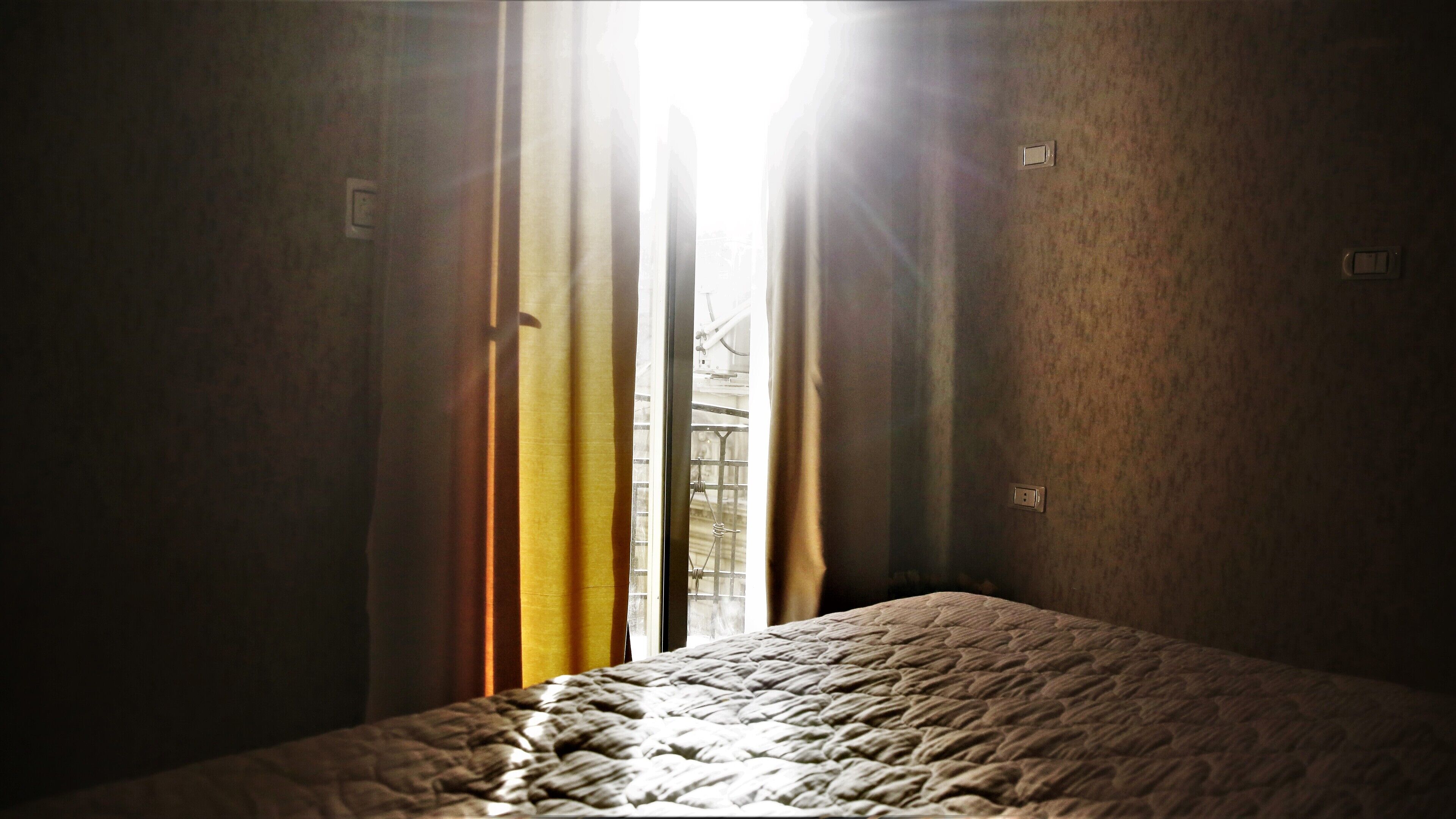 A room with a bed, curtains, and a window with sunlight streaming through.