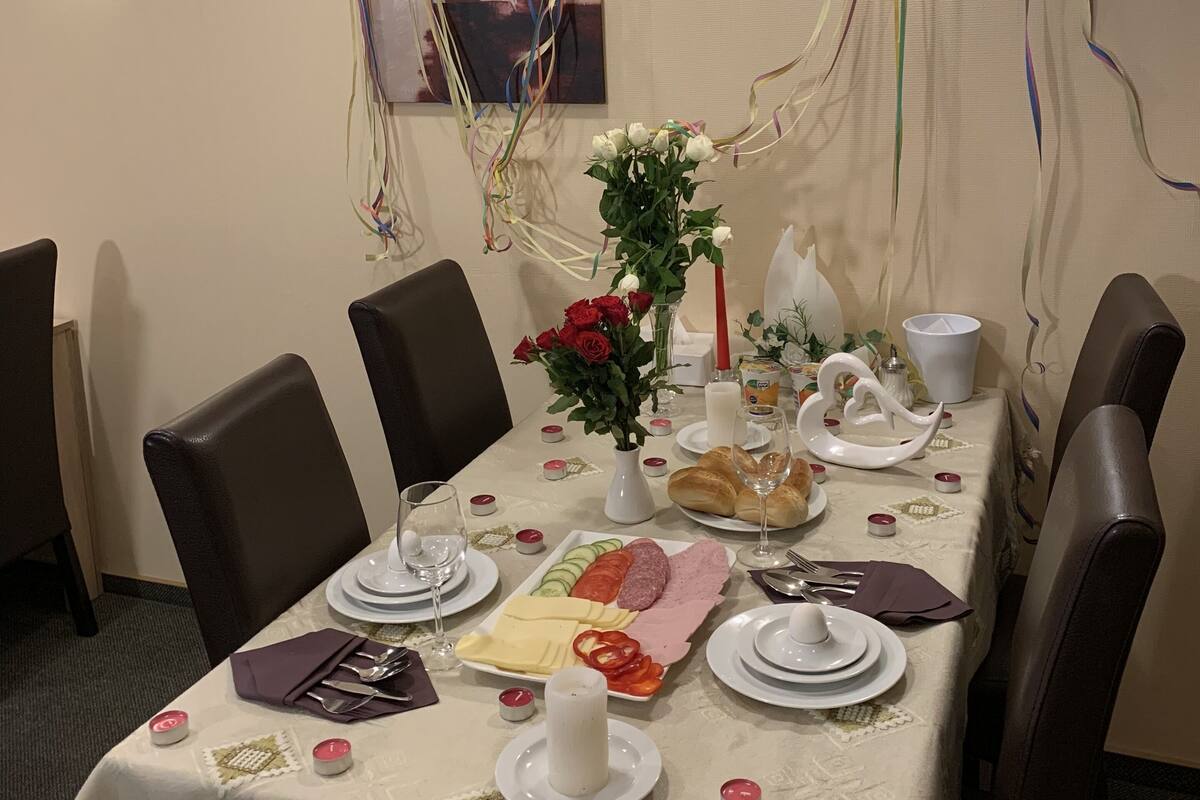 Une table à manger dressée avec des assiettes, des couverts, un vase de fleurs et une bougie.