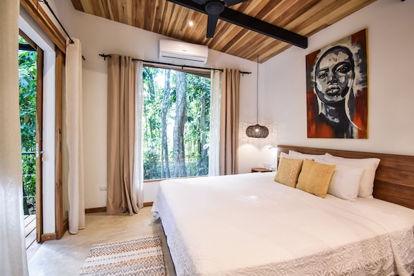 Un dormitorio con una cama grande, ventilador de techo, aire acondicionado, una ventana con cortinas y un cuadro en la pared.