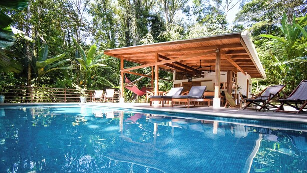 A pool area with lounge chairs and a wooden pergola. - Satta Lodge (Cahuita)