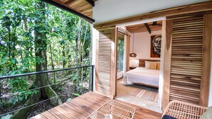 A wooden deck with a glass table, a bed with a white bedspread, and a painting on the wall. - Satta Lodge (Cahuita)
