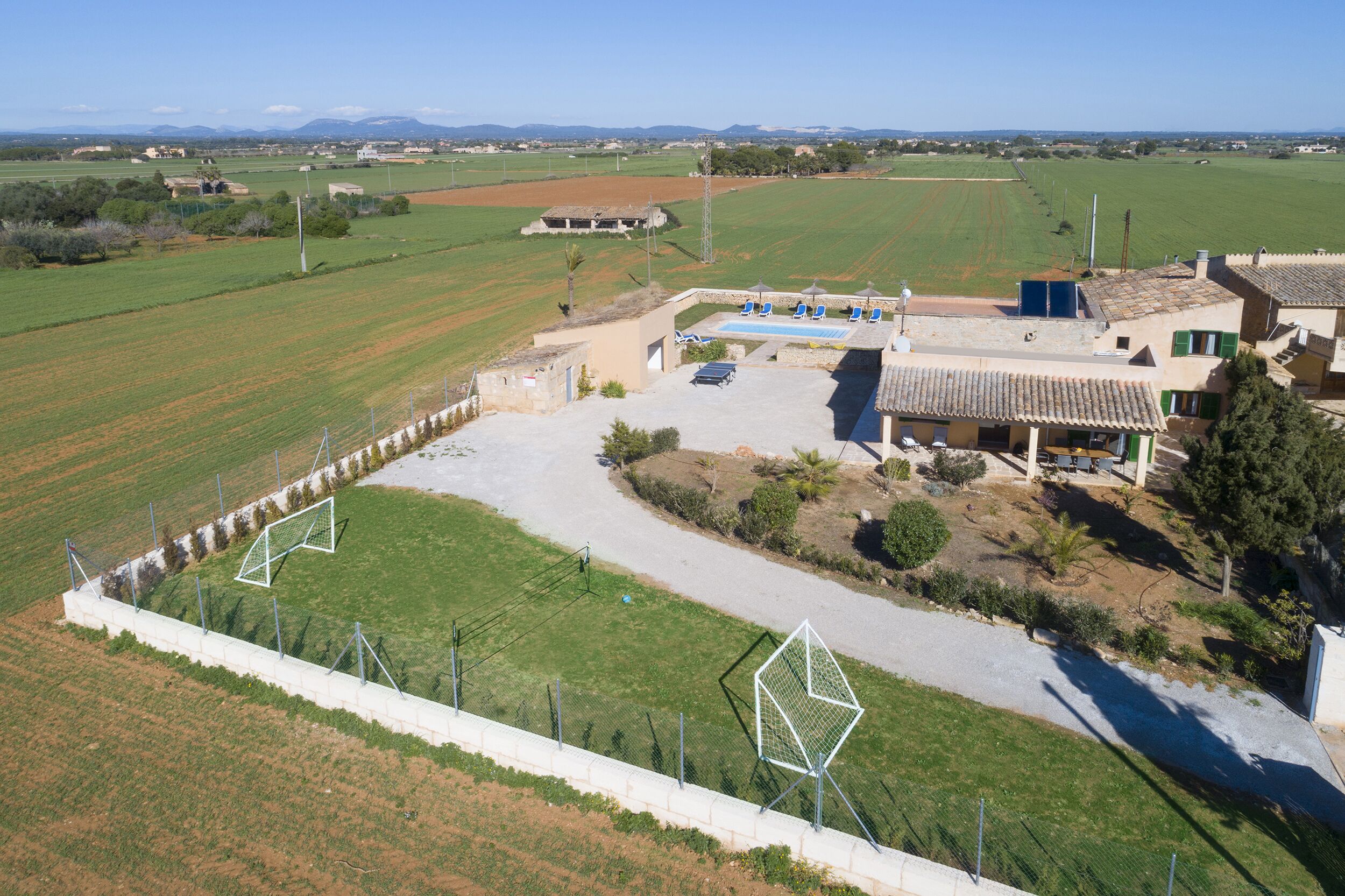 Una extensa propiedad con piscina, mobiliario exterior y un campo deportivo cercado.