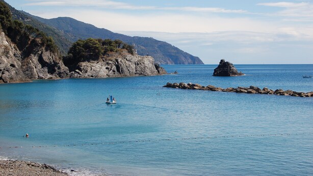 Un paysage côtier avec des falaises rocheuses, une mer calme et un petit bateau.