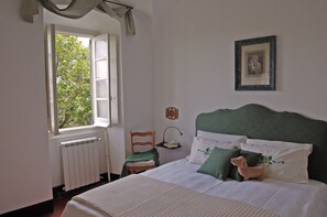 Une chambre bien rangée, avec un lit, une chaise, un radiateur et une fenêtre donnant sur un paysage verdoyant.