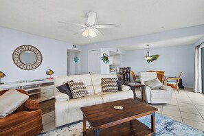 A living room with a sofa, armchairs, a coffee table, a ceiling fan, and a dining area with chairs and a table.