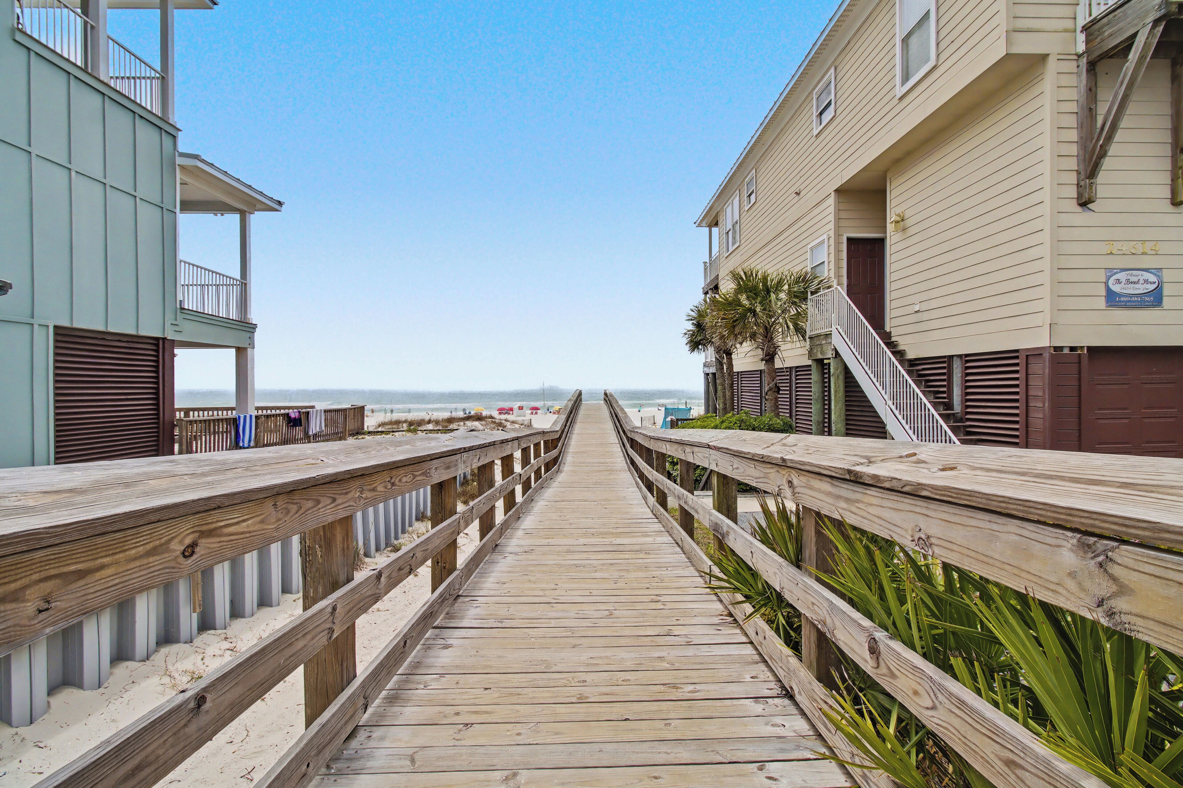 A wooden boardwalk leading to beachfront buildings with balconies and a clear sky.