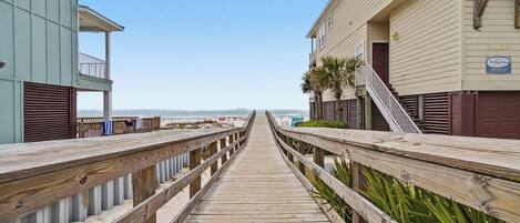 A wooden boardwalk leading to beachfront buildings with balconies and a clear sky.