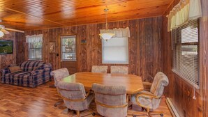 A wooden interior with a dining table, chairs, a sofa, and a ceiling fan.