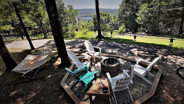 A cozy outdoor seating area with Adirondack chairs, a hammock, and a fire pit, overlooking a scenic landscape.