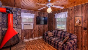 A cozy cabin interior with a wooden ceiling, a red chimney, a plaid sofa, and a mounted TV.