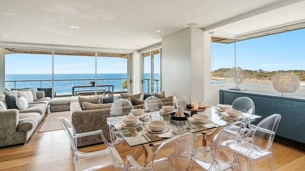 Un'area pranzo moderna con sedie trasparenti in vetro e un tavolo imbandito per sei persone, con vista panoramica sull'oceano.