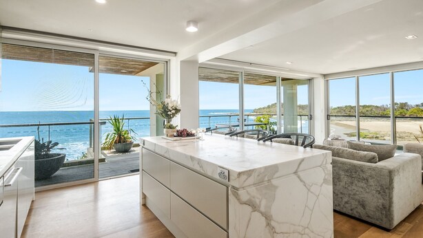 Een moderne keuken met een groot eiland, een eethoek met uitzicht op het strand en een zithoek met uitzicht op de oceaan.