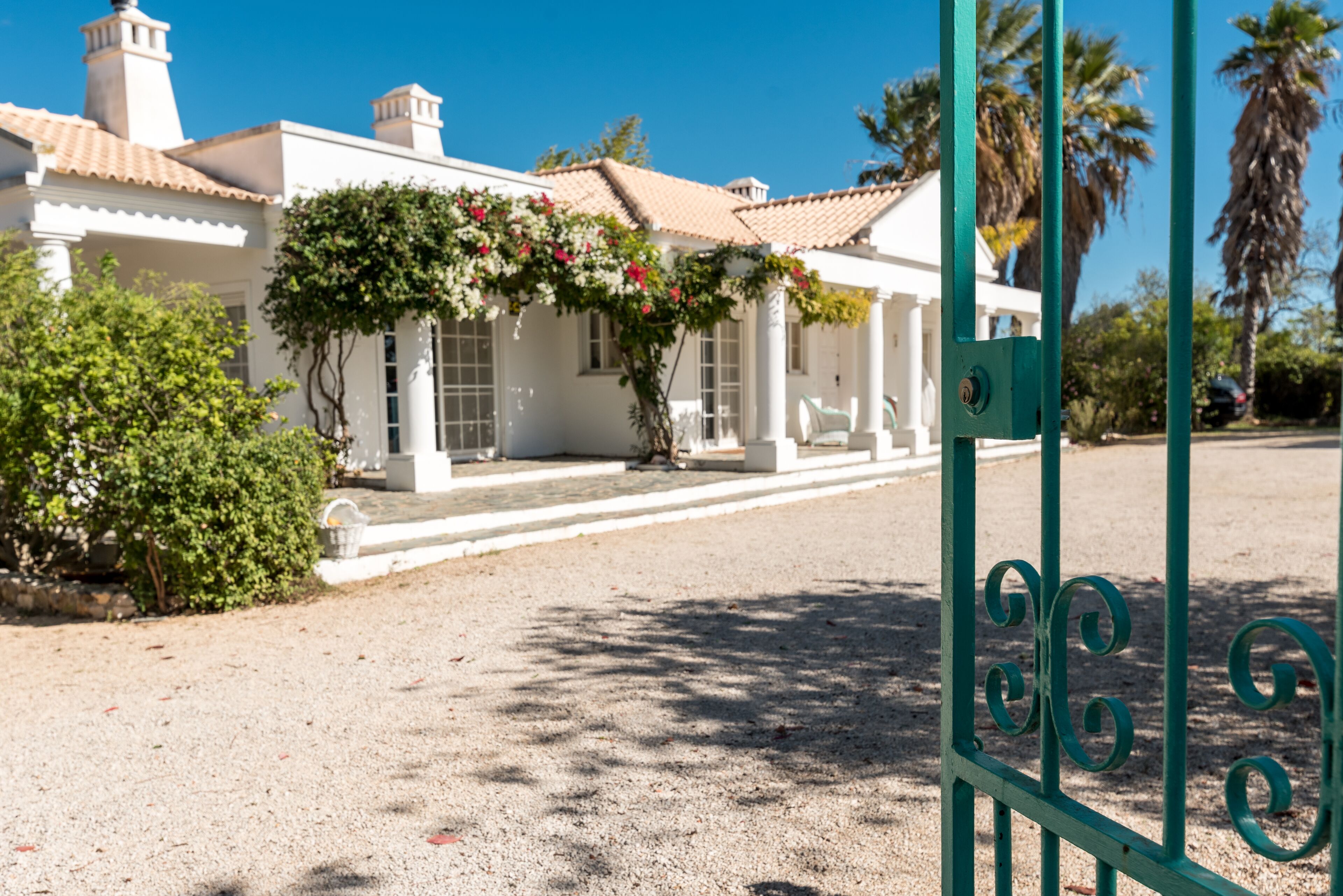 A white building with a tiled roof, a covered porch, and a gravel driveway.