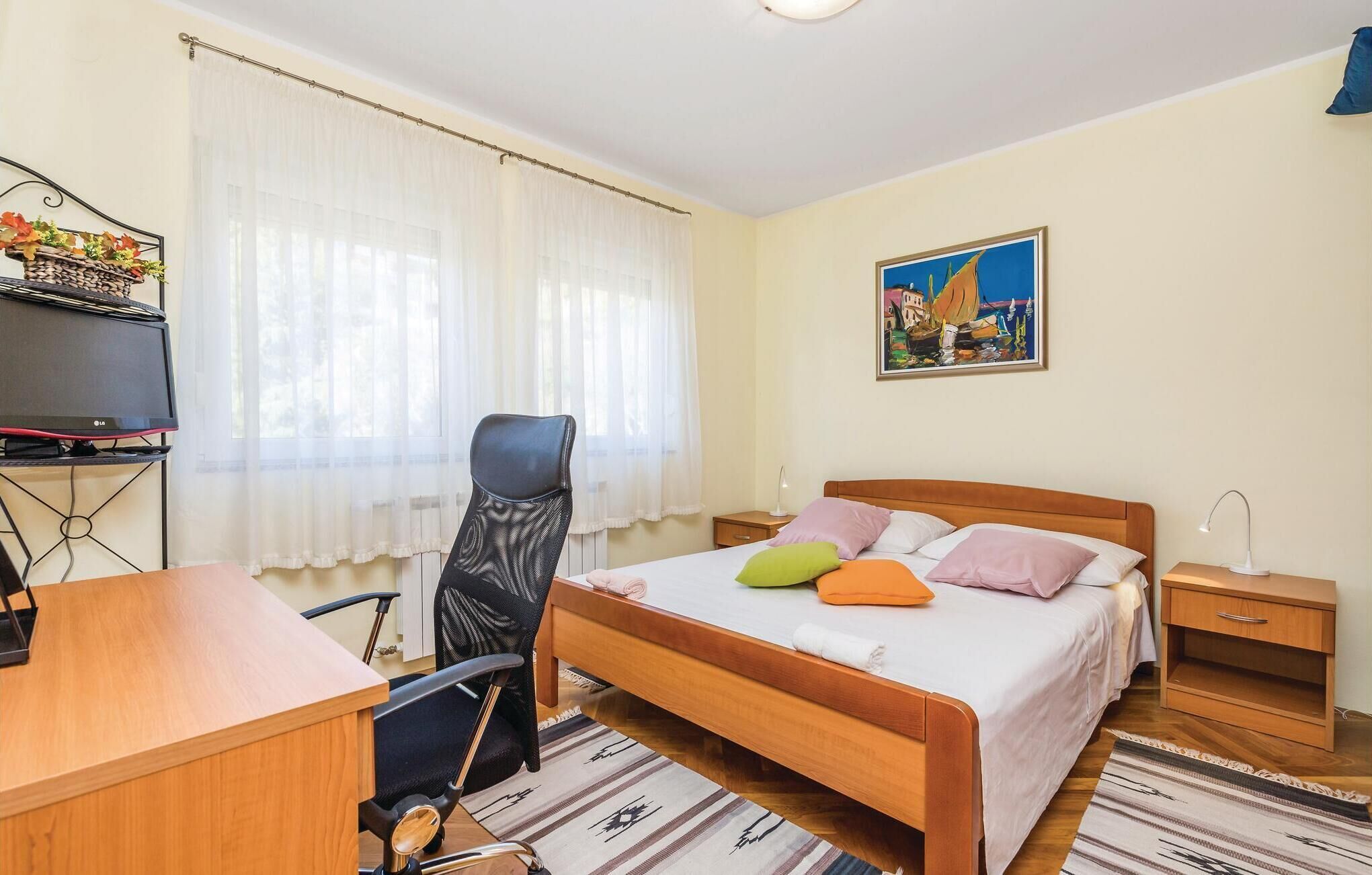 A hotel room with a wooden bed, a desk with a computer, a chair, a nightstand, and a painting on the wall.