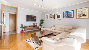 A modern living room with a beige sofa, a glass coffee table, a flat-screen TV, and a wooden cabinet. There are four framed artworks on the wall and a potted plant on the floor. - Beautiful apartment in Rijeka with house sea view (Rijeka)