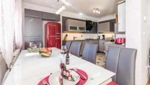 A modern kitchen with grey cabinets, a red refrigerator, and a dining area with a white table set for two. - Beautiful apartment in Rijeka with house sea view (Rijeka)