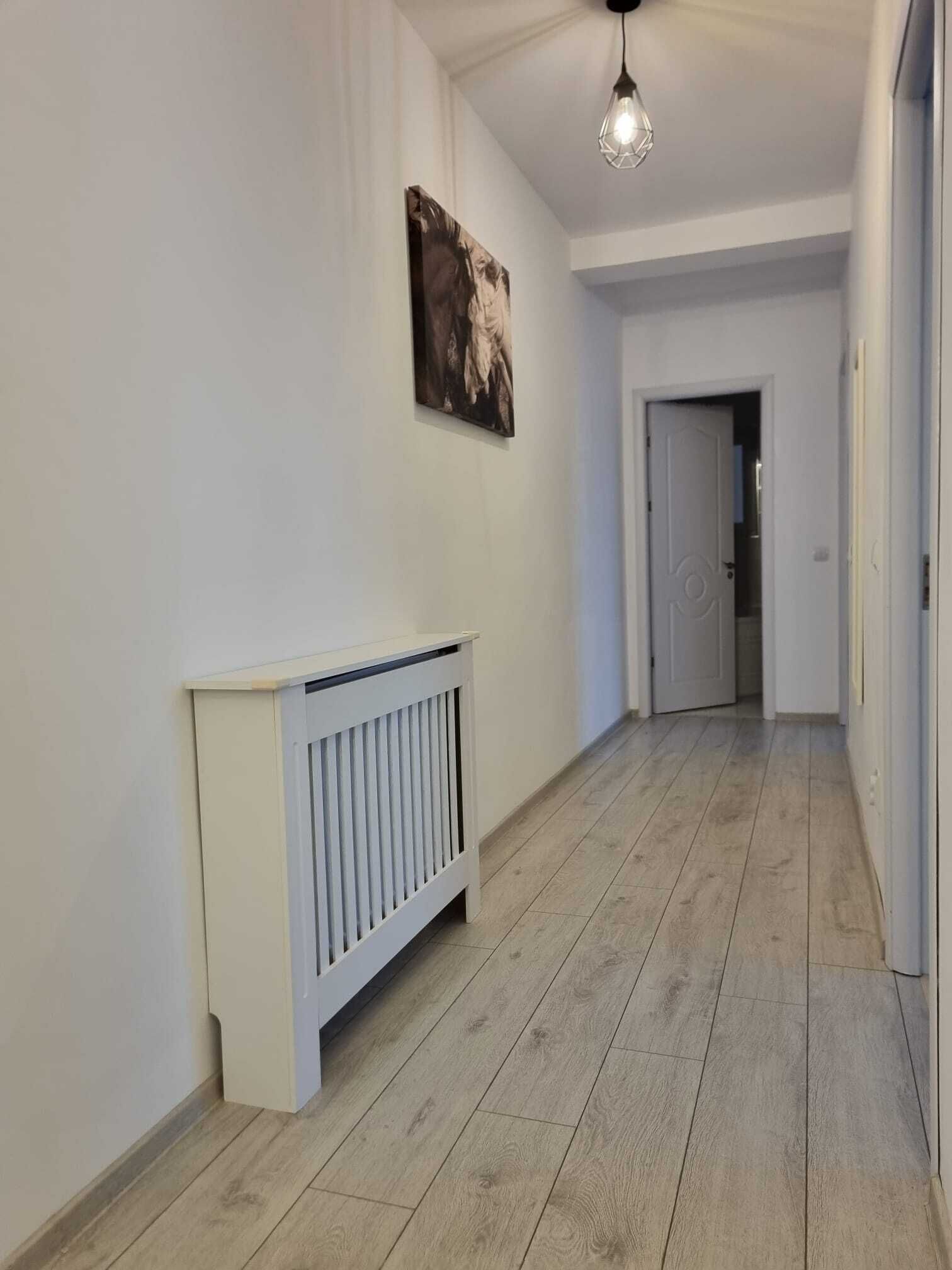 A hallway with a radiator, a door at the end, and a hanging light fixture.
