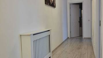 A hallway with a radiator, a door at the end, and a hanging light fixture.