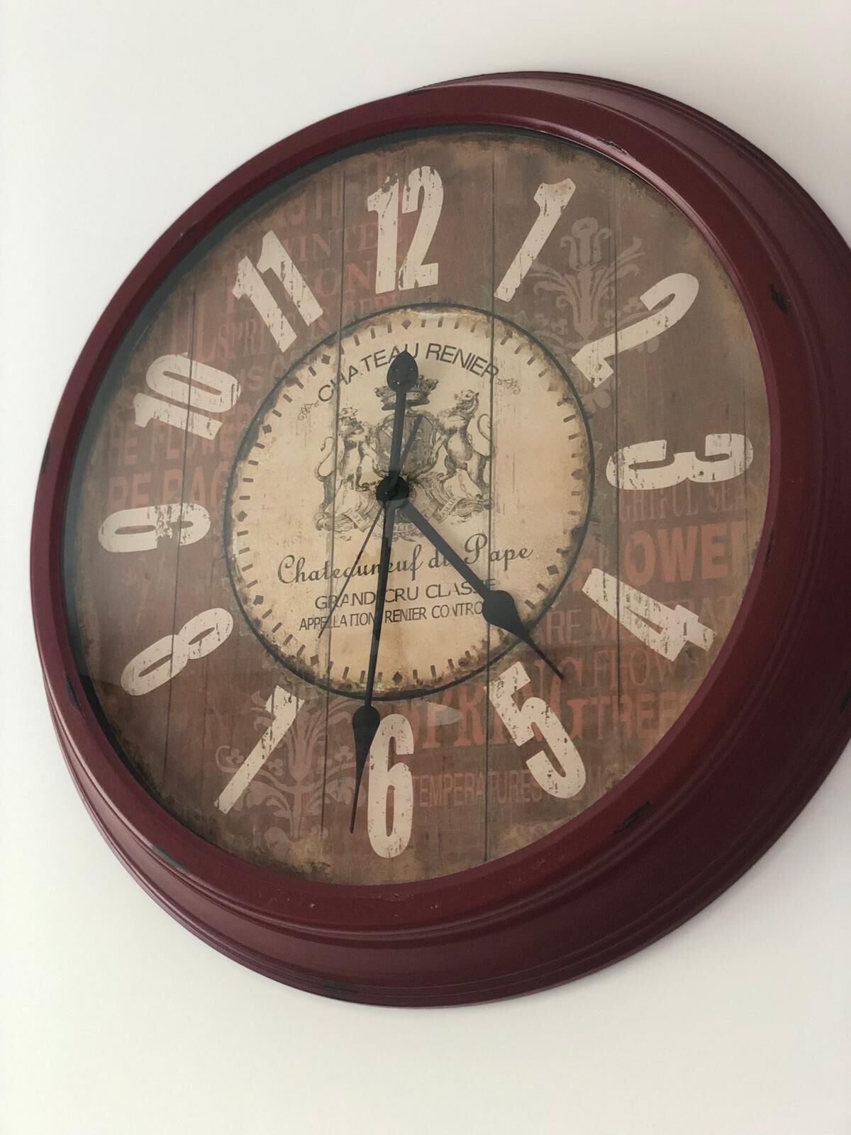 A vintage wall clock with a wooden frame and a glass face, featuring ornate designs and text.