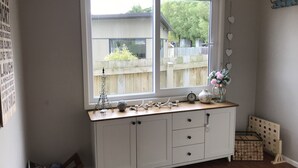 Une pièce d’angle avec une armoire blanche, une fenêtre donnant sur une clôture en bois et de la verdure, et une petite étagère ornée d’objets décoratifs.