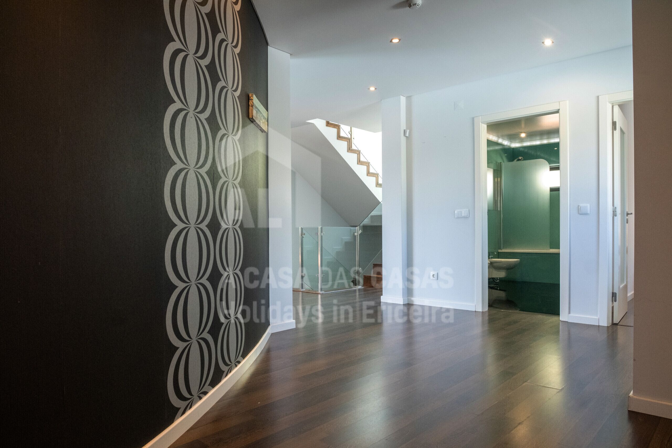 Un intérieur moderne avec un escalier, une salle de bain dotée d’un mur vert et un motif décoratif sur un autre mur.