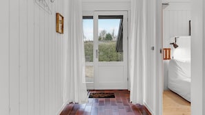 A narrow hallway with white walls, a wooden door with a window, and a bed with a wooden headboard in the adjacent room. - 3 bedroom cozy home in Sydals (Sydals)