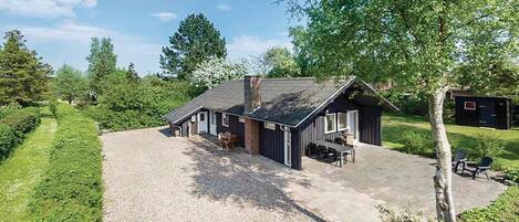 A two-story house with a gravel driveway, a patio with outdoor furniture, and a small shed in the background.