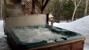 Ein Whirlpool in einer verschneiten Winterlandschaft mit einer Holzterrasse und Treppe.