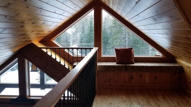 Ein Dachzimmer aus Holz mit schrägem Dach, einem Fenster und einer kleinen Bank mit Kissen.