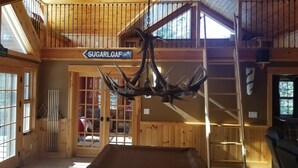 Ein rustikales Blockhaus-Interieur mit einem großen Wandleuchter aus Geweihen, Holzwänden und einem Schild mit der Aufschrift 'Sugarloaf'.
