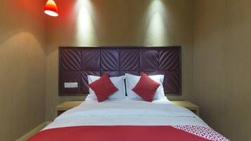 A hotel room with a large bed, a headboard with a diamond pattern, and two red pillows.