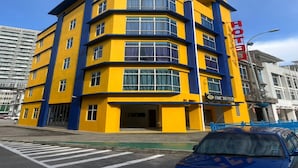 A corner hotel with a yellow and blue facade, multiple floors, and a visible entrance.