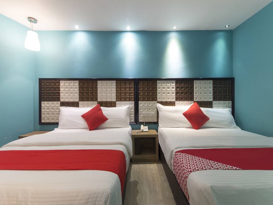 A hotel room with two beds, each with a red and white bedspread, a wooden nightstand with a phone, and a blue accent wall.