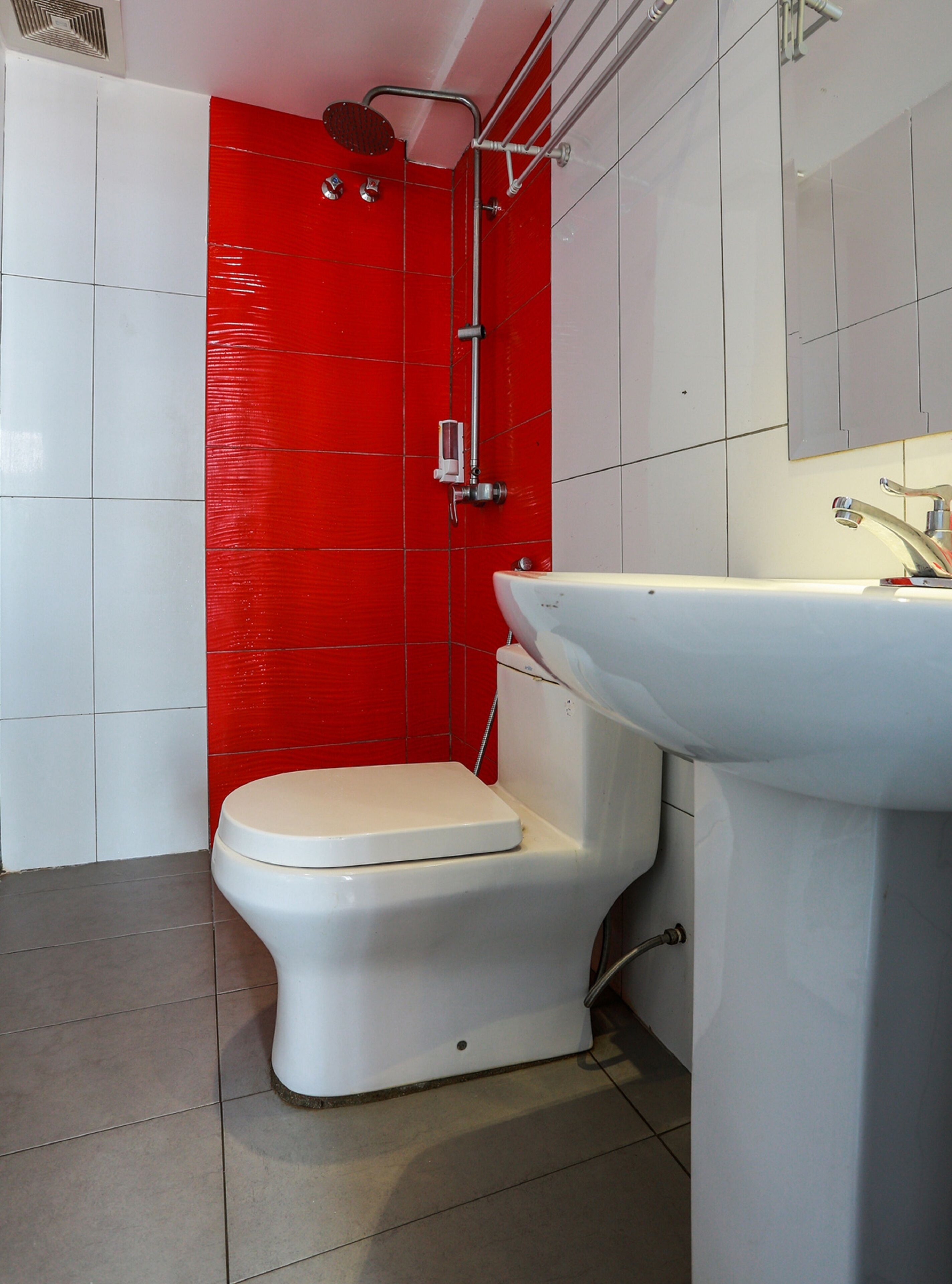 A bathroom with a white toilet, a white sink, and a red shower enclosure.