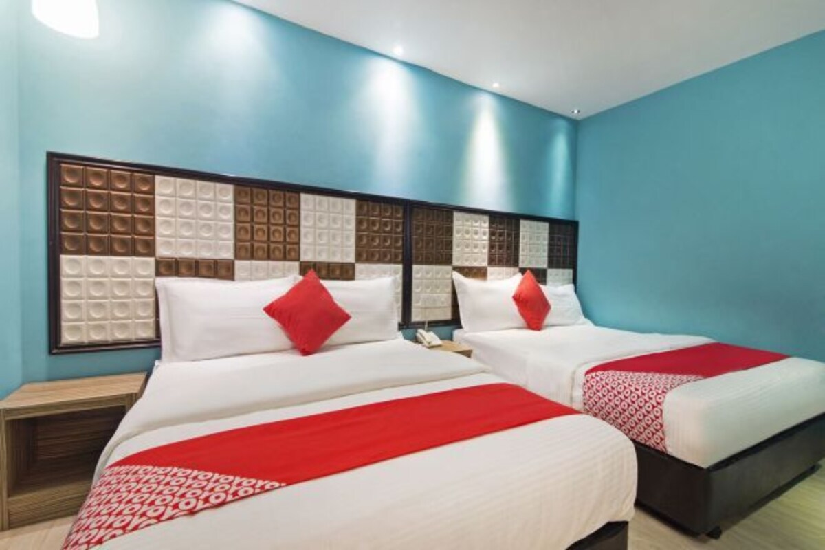 Quarto de hotel com duas camas, uma cabeceira decorativa grande e uma parede azul.