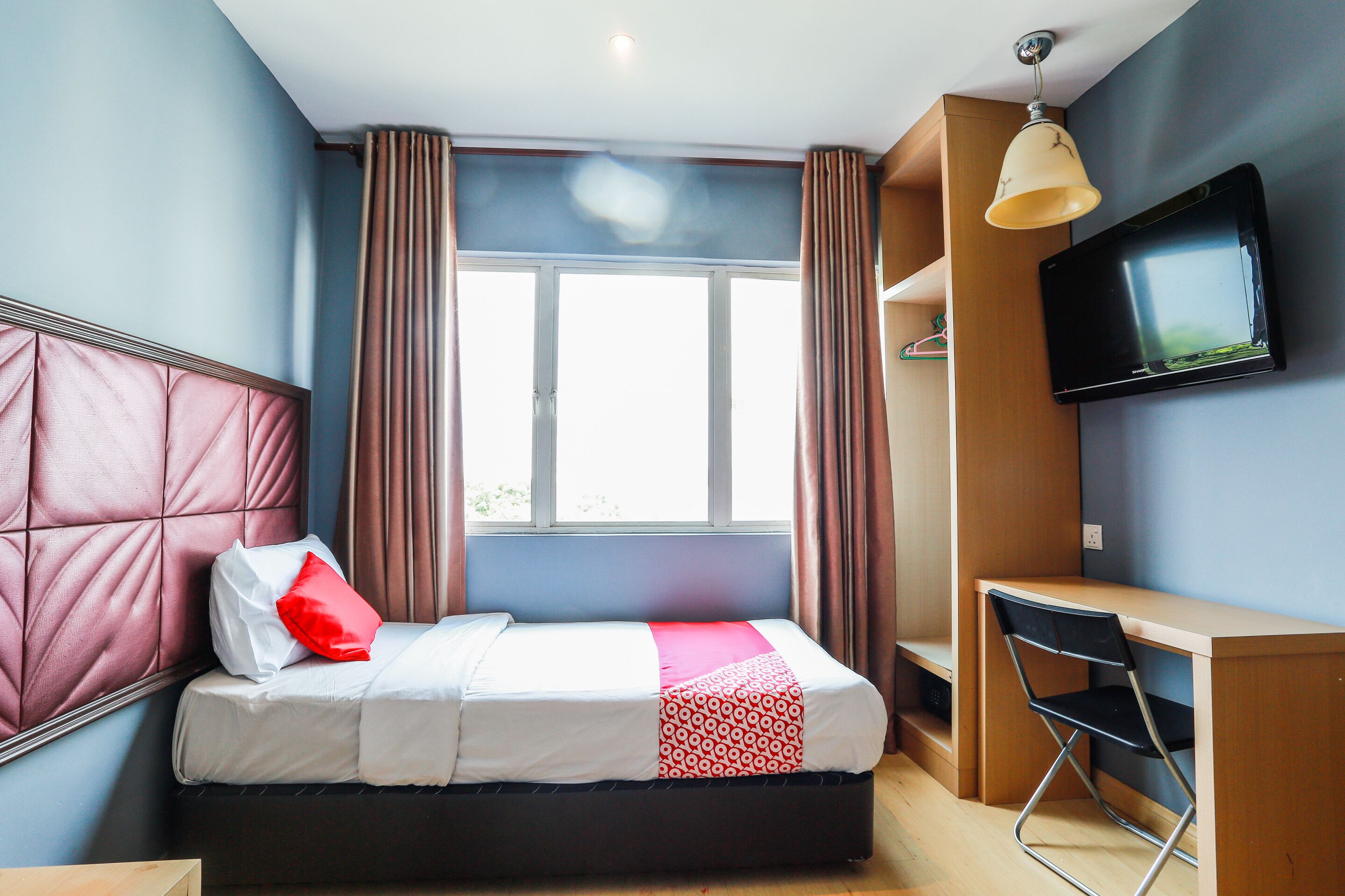 Un dormitorio con cama, escritorio, silla, televisor y ventana con cortinas.
