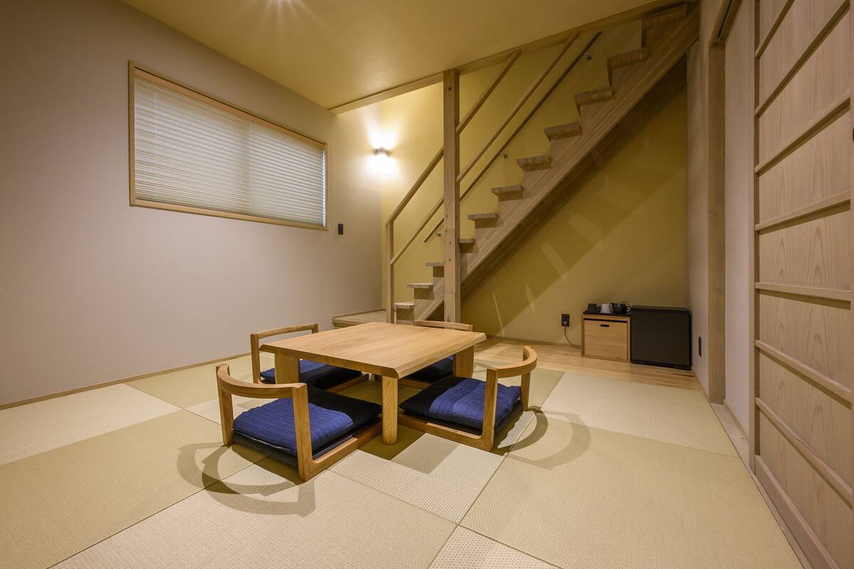 A traditional Japanese room with tatami flooring, a low wooden table with cushions, a built-in shelf, and a staircase.