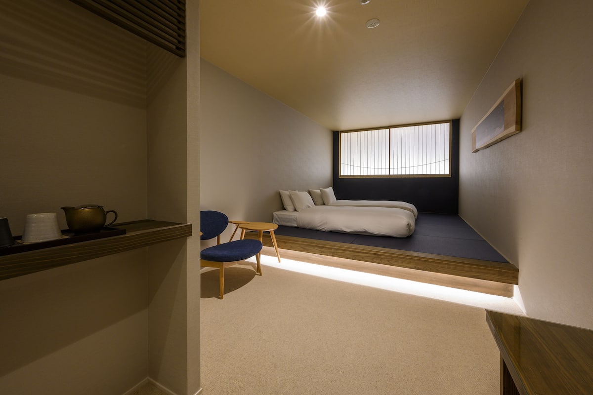A compact bedroom with a built-in bed, a small seating area, and a window providing natural light.