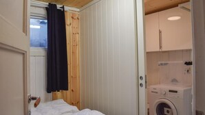 Una habitación pequeña y funcional con cama, lavadora y ventana con cortina.