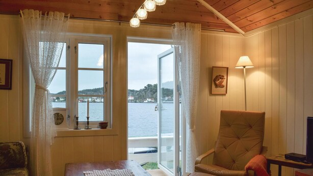 Una habitación acogedora con techo de madera, una silla con cojín, una mesa y vistas a un cuerpo de agua a través de una ventana.