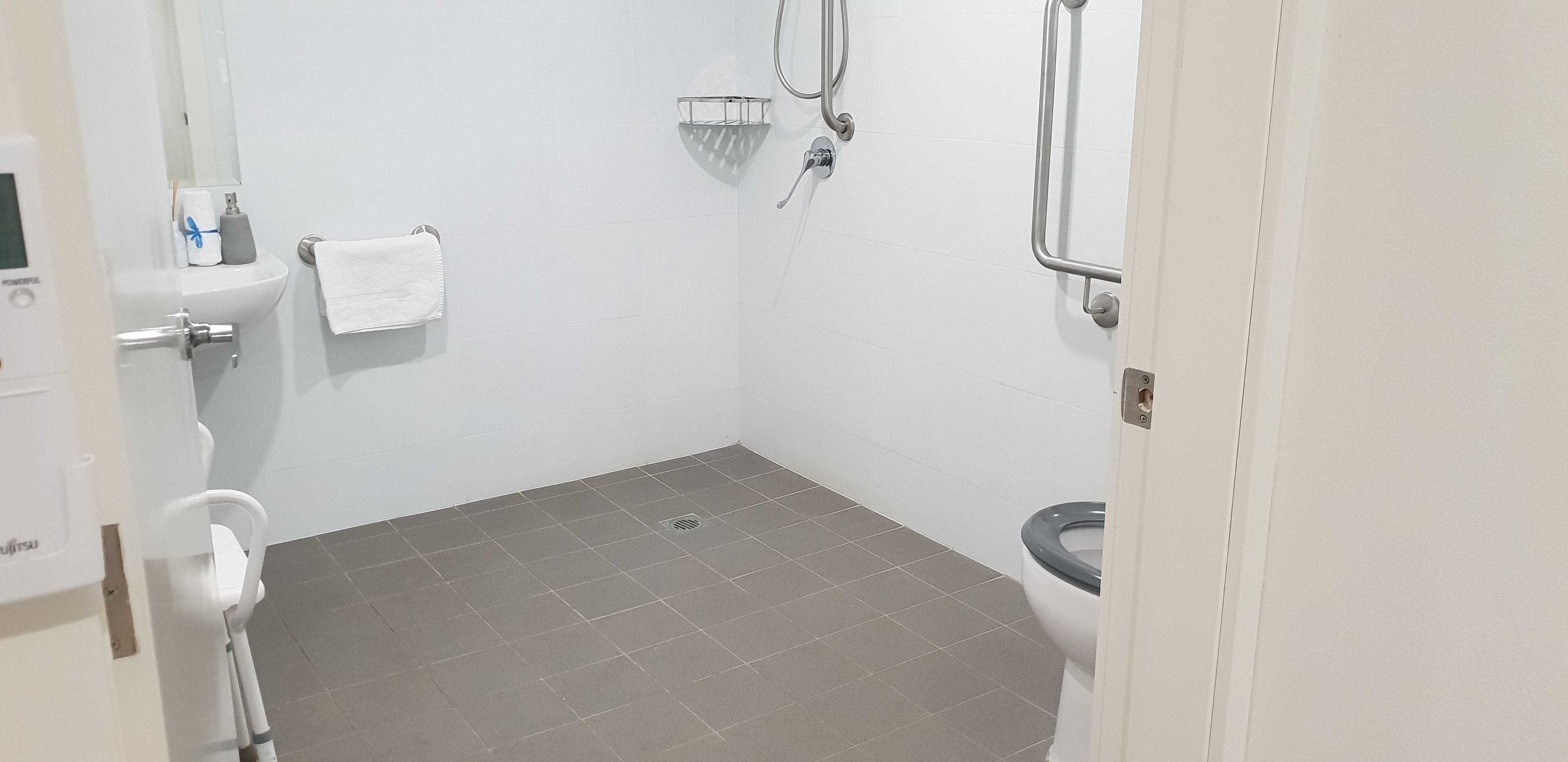 Une petite salle de bain propre, équipée de toilettes, d’une douche et d’une barre d’appui.