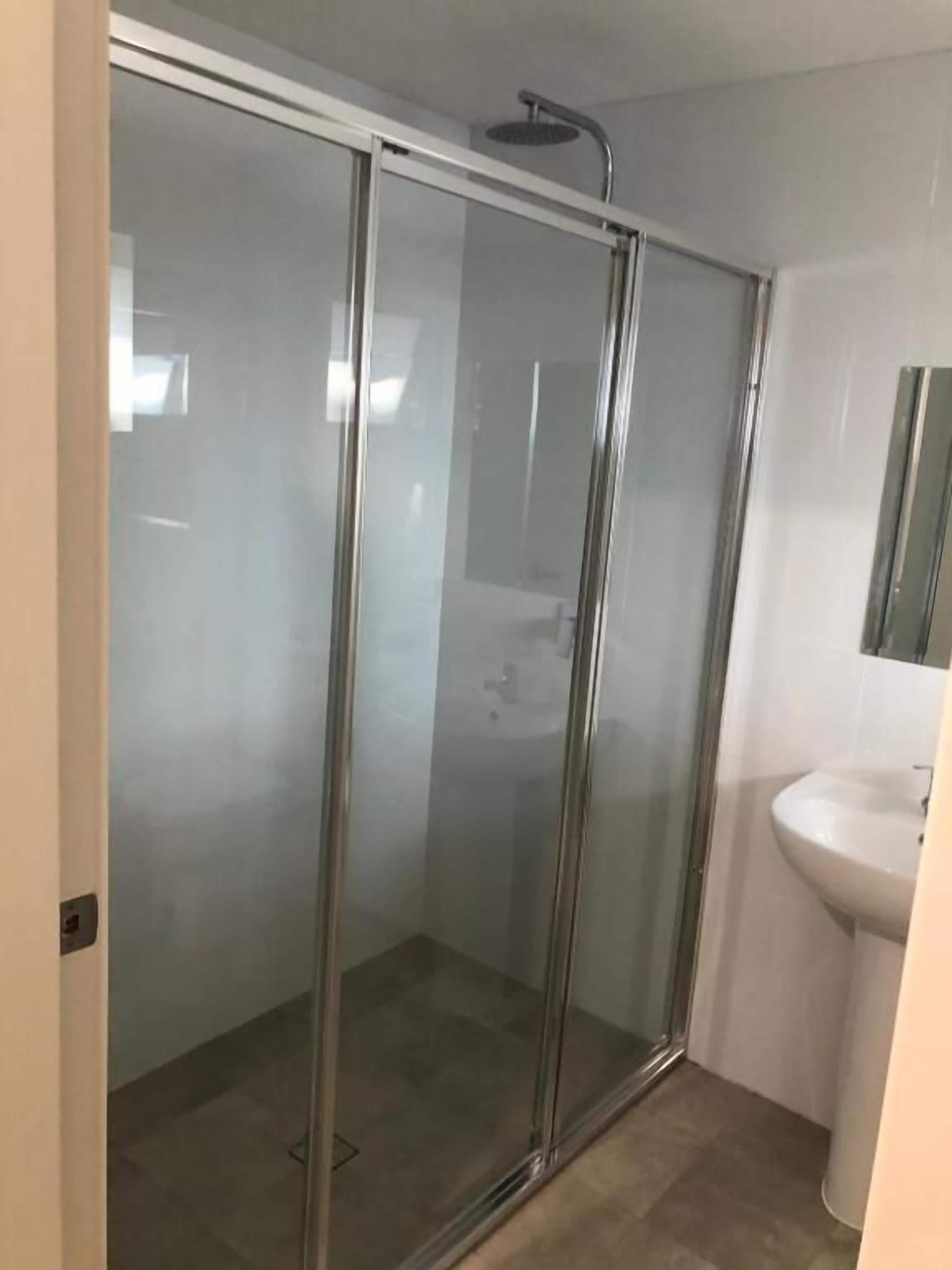 A glass-enclosed shower stall with a white sink and mirror in a bathroom.