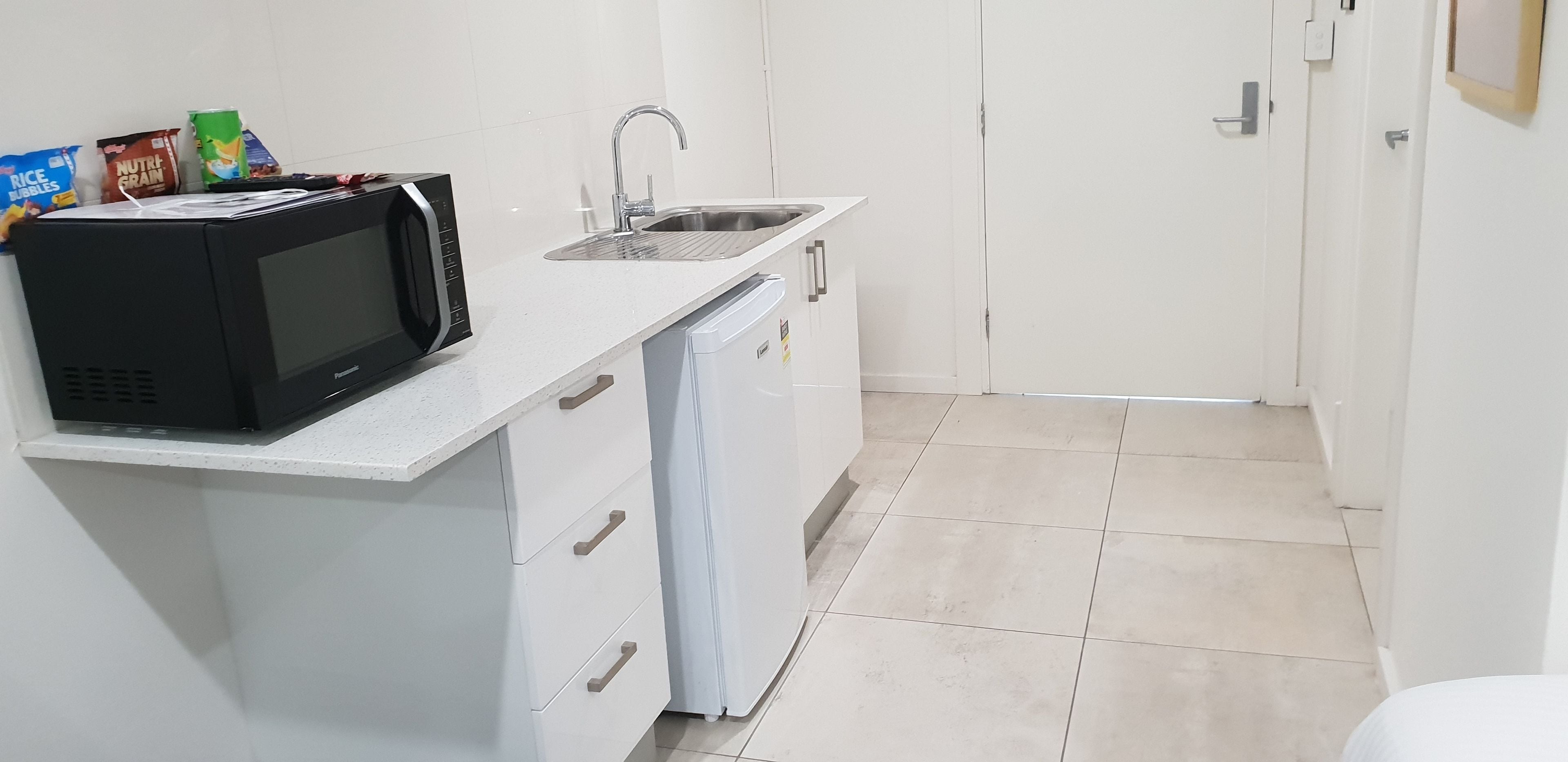A compact kitchen with a microwave, sink, and a small refrigerator.
