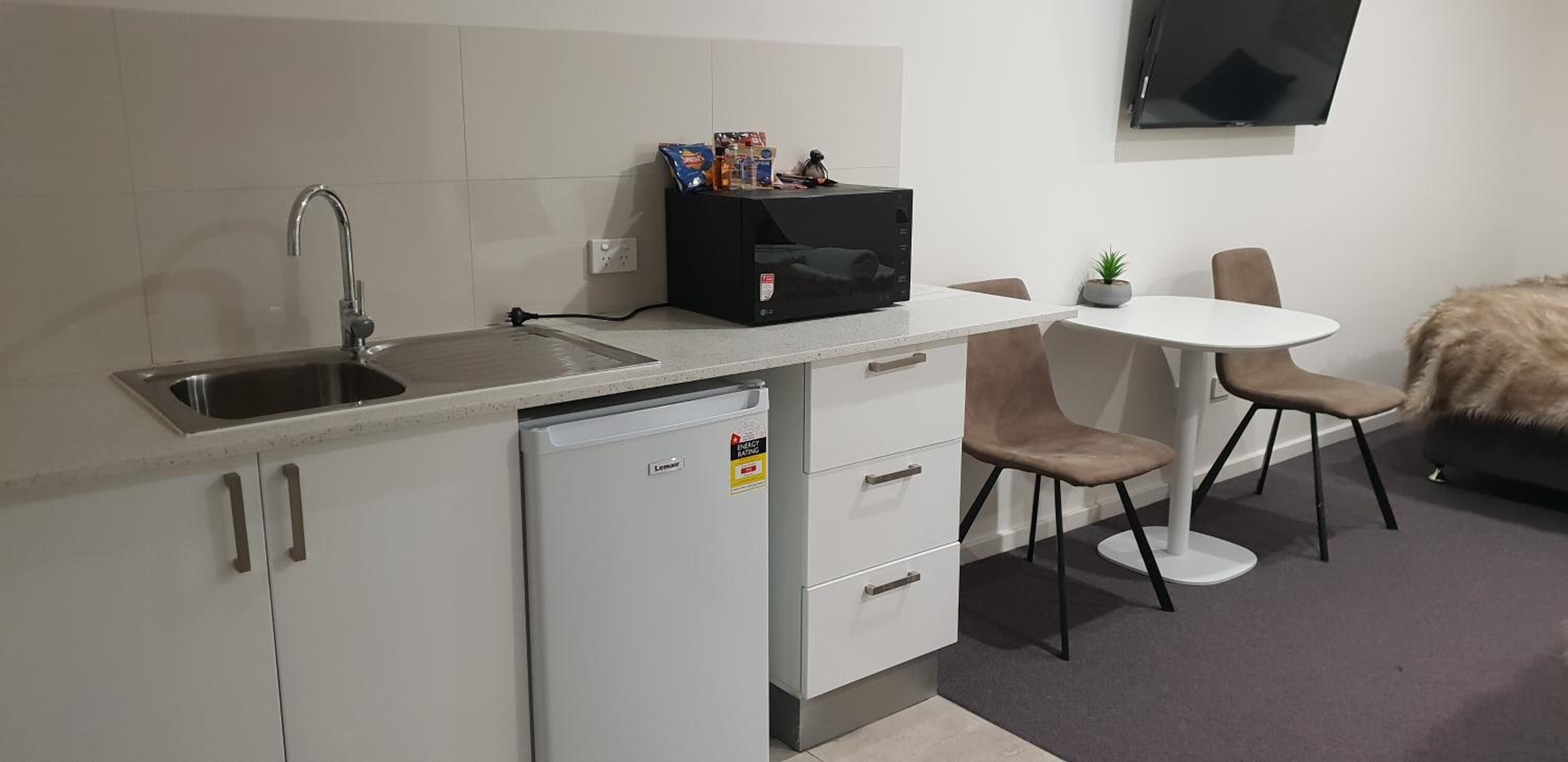 A compact kitchenette with a sink, a small refrigerator, a microwave, and a dining area with a table and chairs.