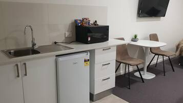 A compact kitchenette with a sink, a small refrigerator, a microwave, and a dining area with a table and chairs.