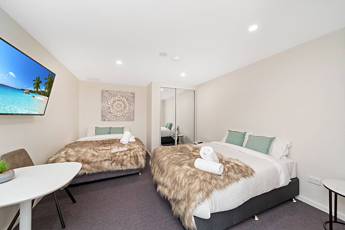 A hotel room with two beds, a TV, a mirror, and a small table.